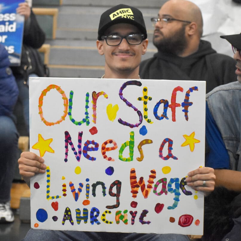 A self advocate holds a sign in support of higher wages for direct care staff